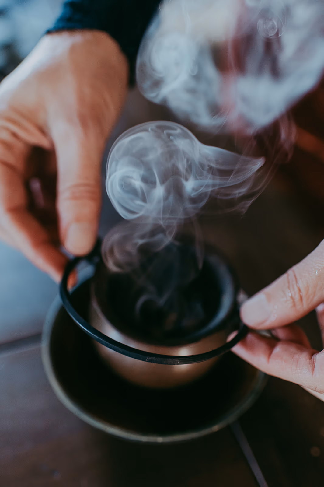 Hands holding a smoking incense burner with swirling aromatic smoke rising.