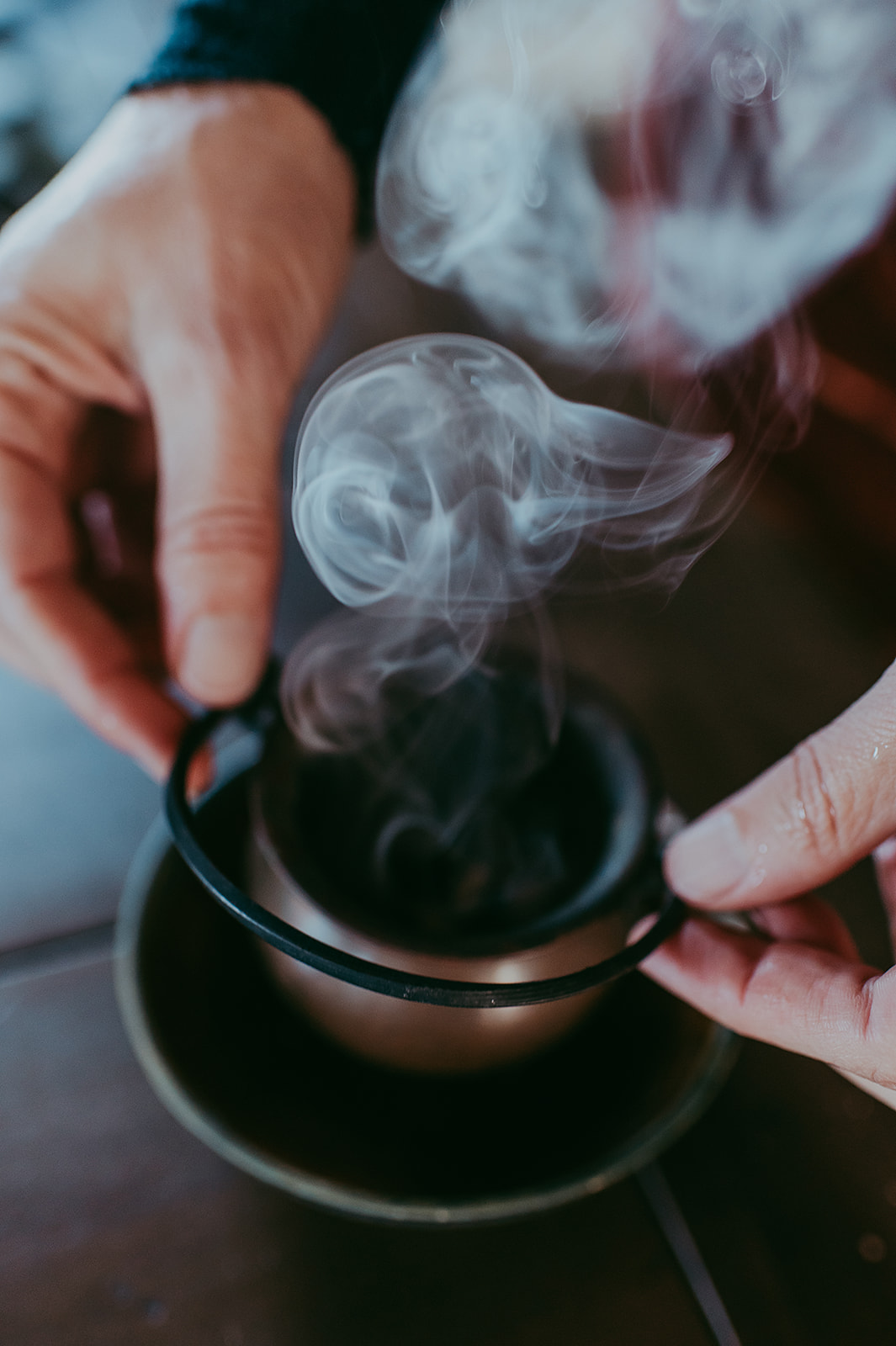 Hands holding a smoking incense burner with swirling aromatic smoke rising.
