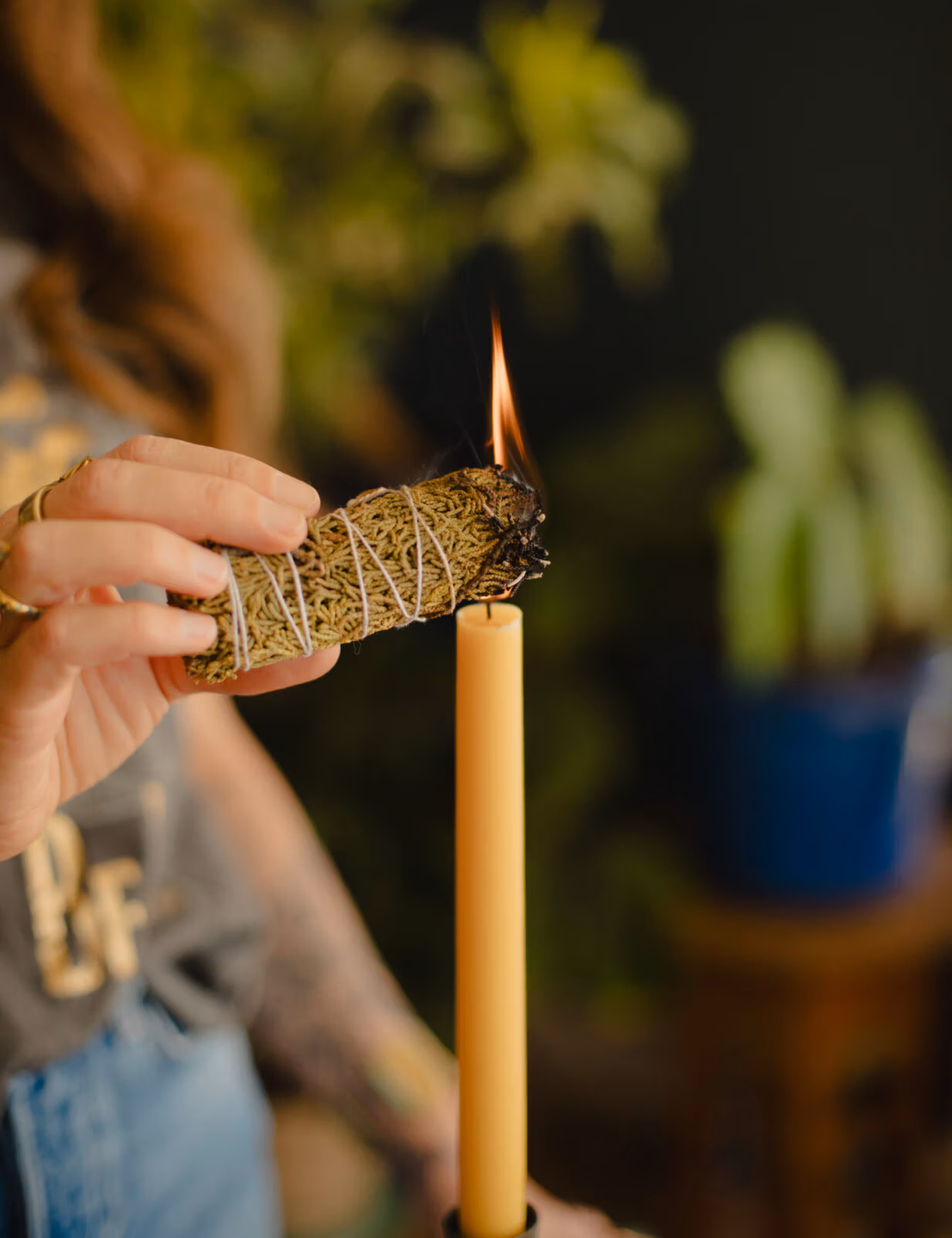 Person lighting a bundle of sage or herbs from a candle flame during a ritual or cleansing practice.