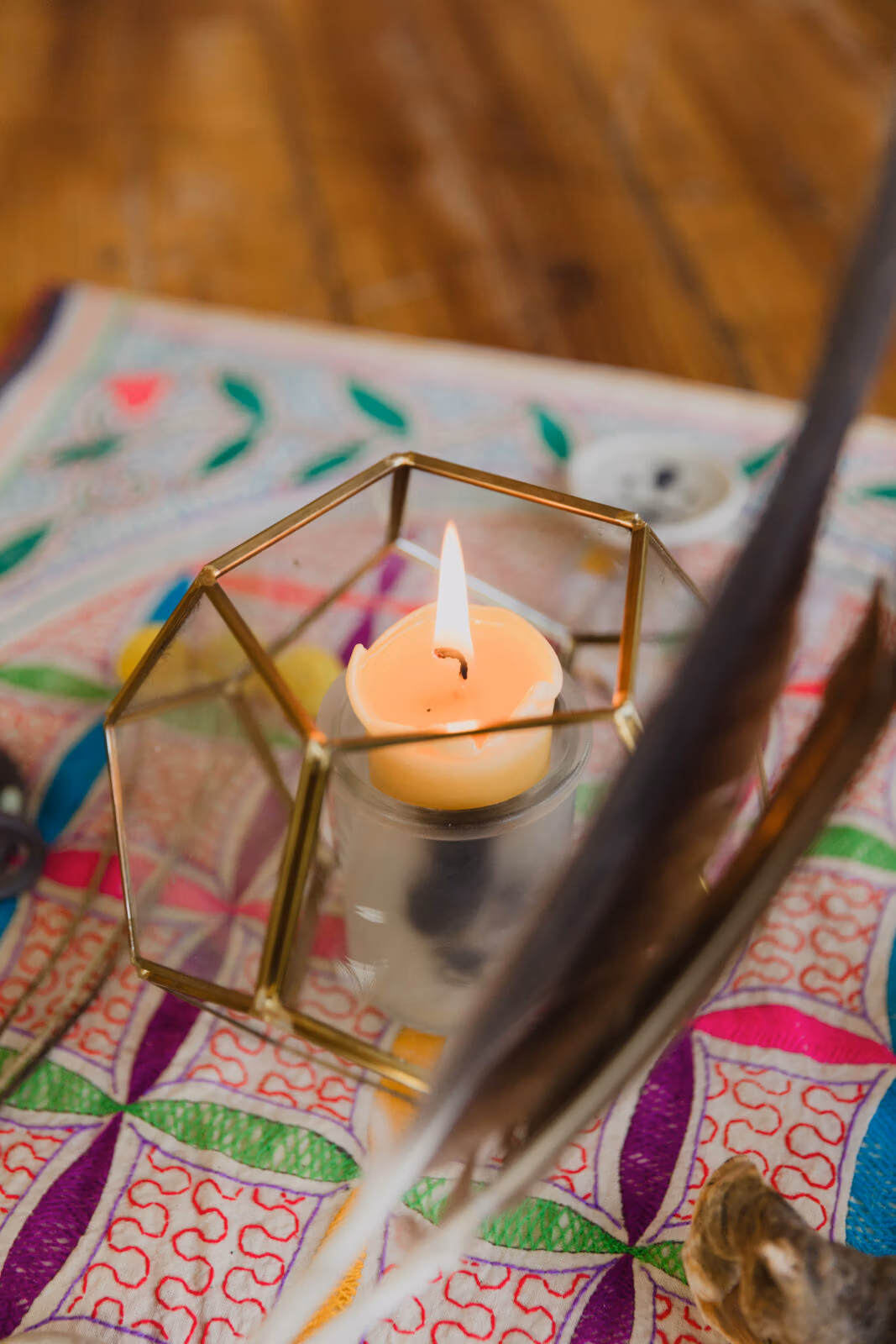 Lit candle in a geometric glass holder placed on a colorful sacred geometry mat.