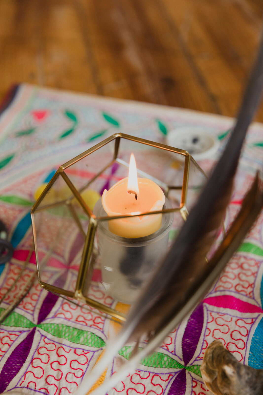 Lit candle in a geometric glass holder placed on a colorful sacred geometry mat.