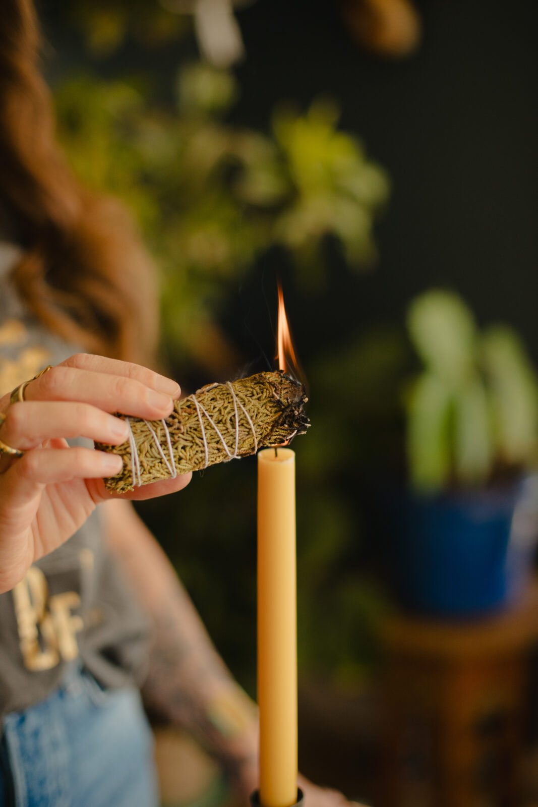 Close-up of a woman (Briana Borten) lighting a sage bundle with a candle during a cleansing ritual